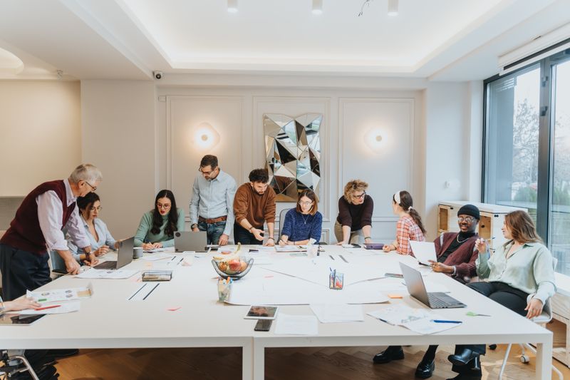 Group of people collaborating and brainstorming ideas around a large table in a bright, modern office environment