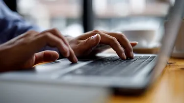 Hands typing on a laptop keyboard on a wooden table.