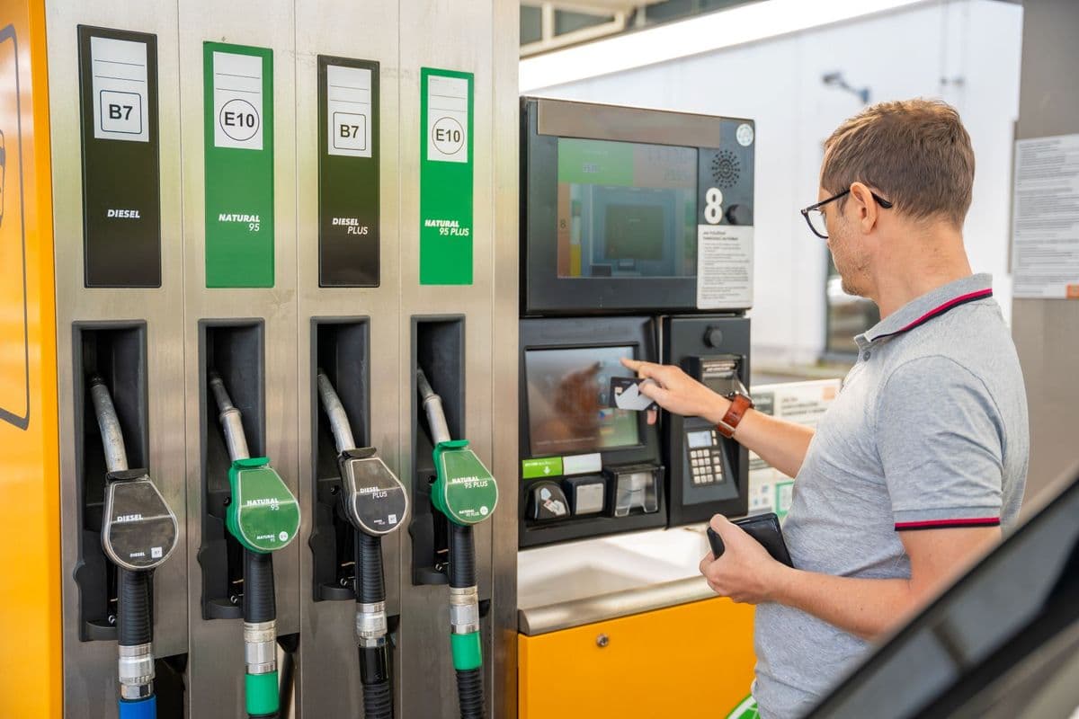 A person uses a touchscreen at a gas station with options for Diesel, Natural 95, Diesel Plus, and Natural 95 Plus fuel.