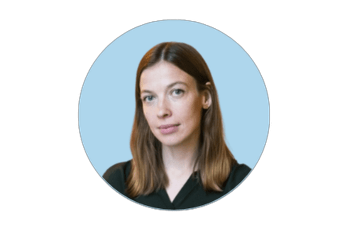 Portrait of a person with shoulder-length brown hair, wearing a dark top, against a light blue circular background.