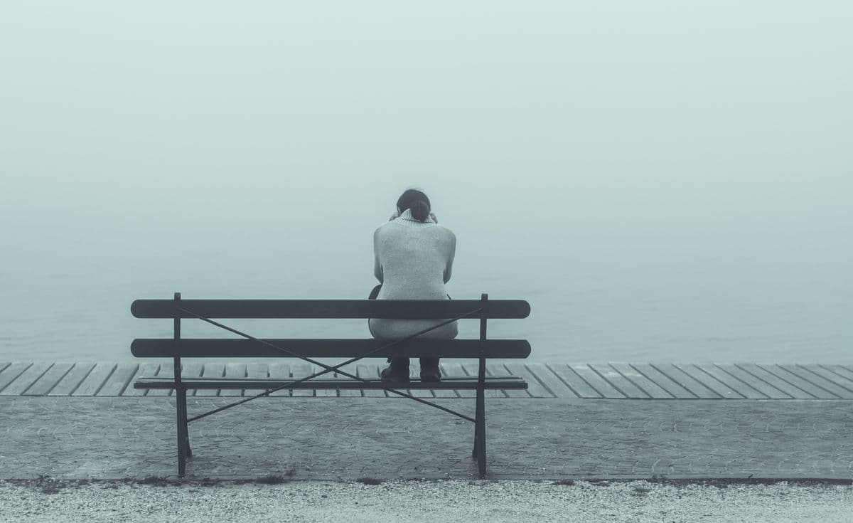Person sitting on bench in front of foggy lake