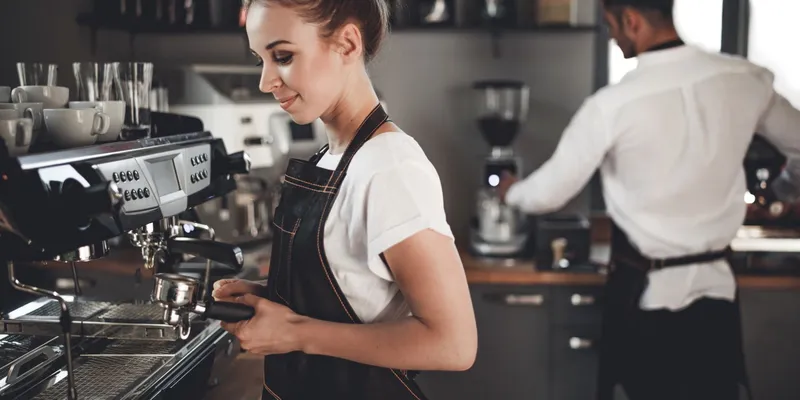 Young barista preparing coffee using a professional coffee machine in a coffee shop