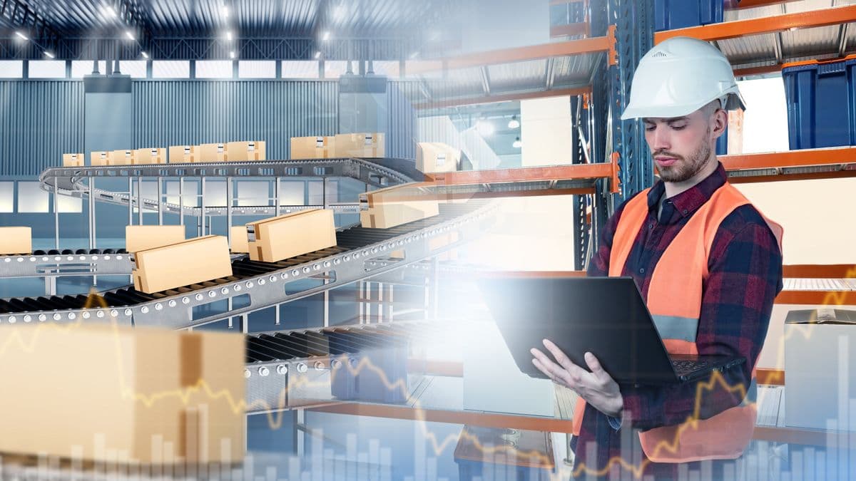 Mail warehouse worker monitors package conveyor system using a laptop.