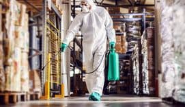 Man in protective suit disinfecting warehouse