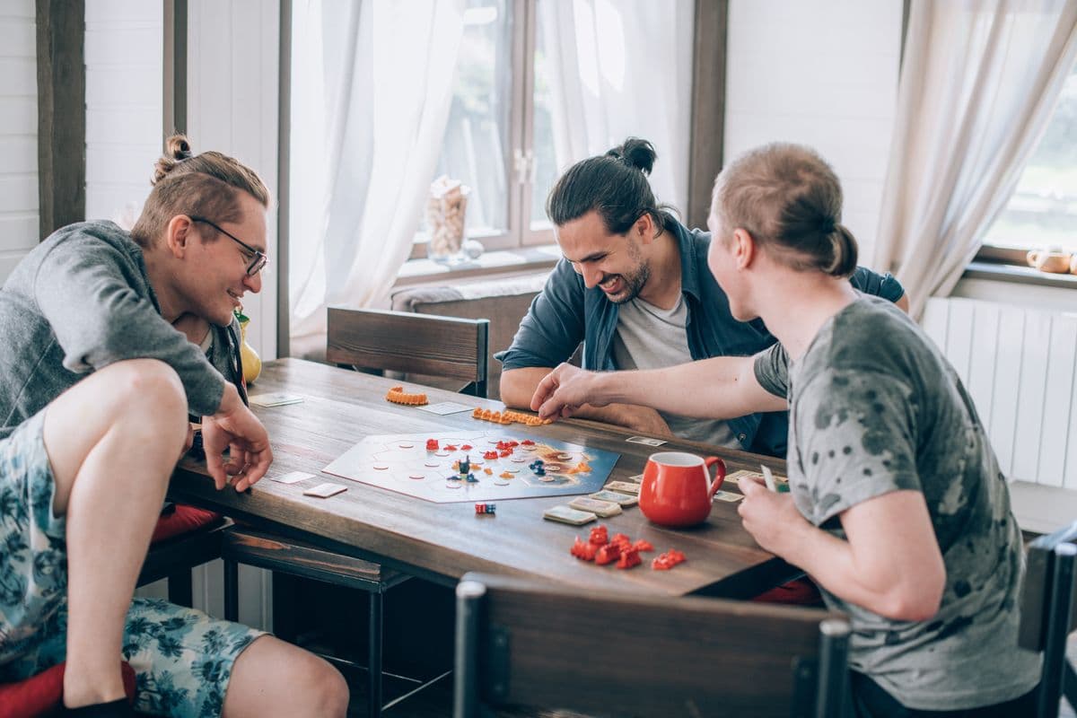 Three male adult friends play a board game in the living room