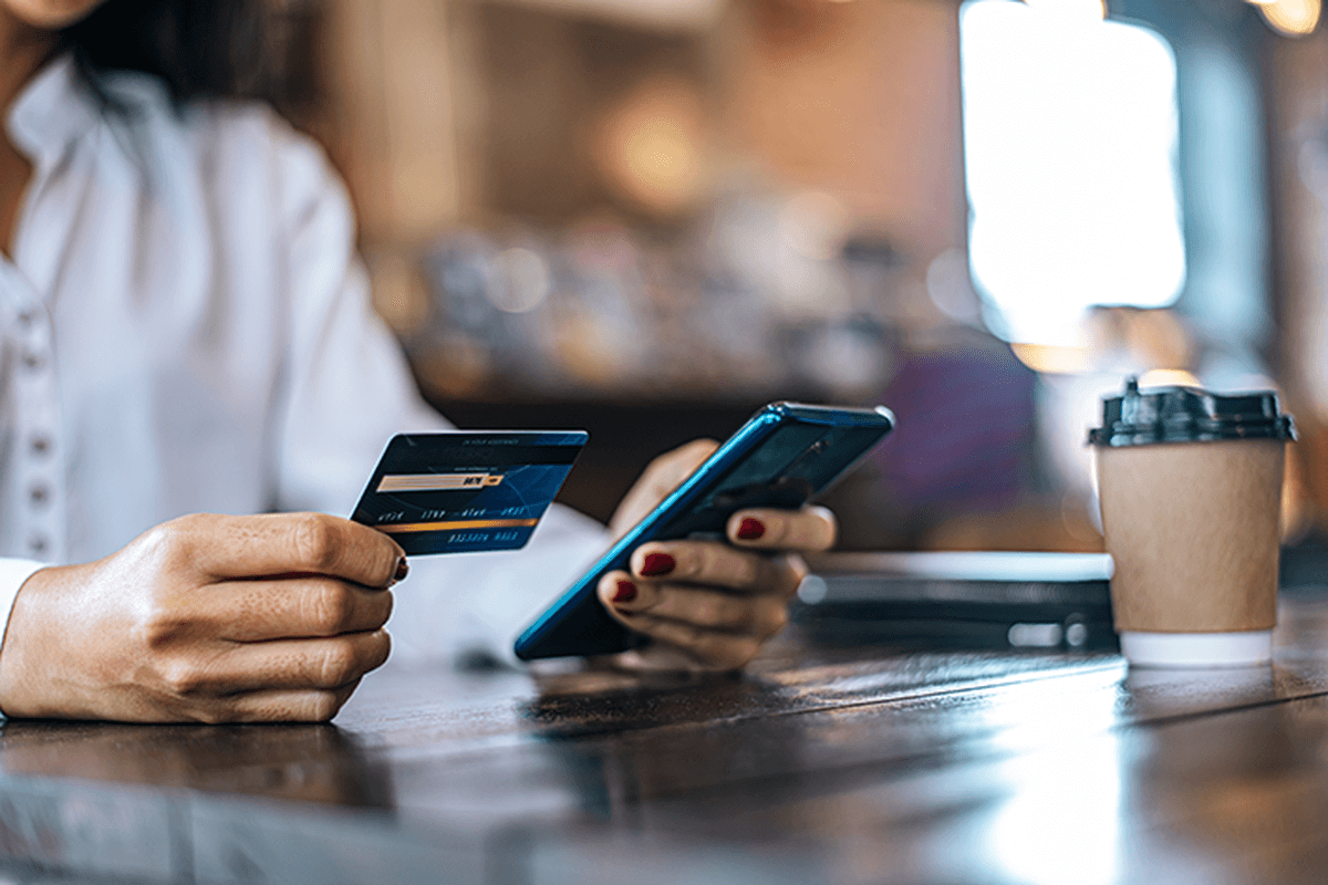 Image of woman paying for goods by credit card through a smartphone in a coffee shop