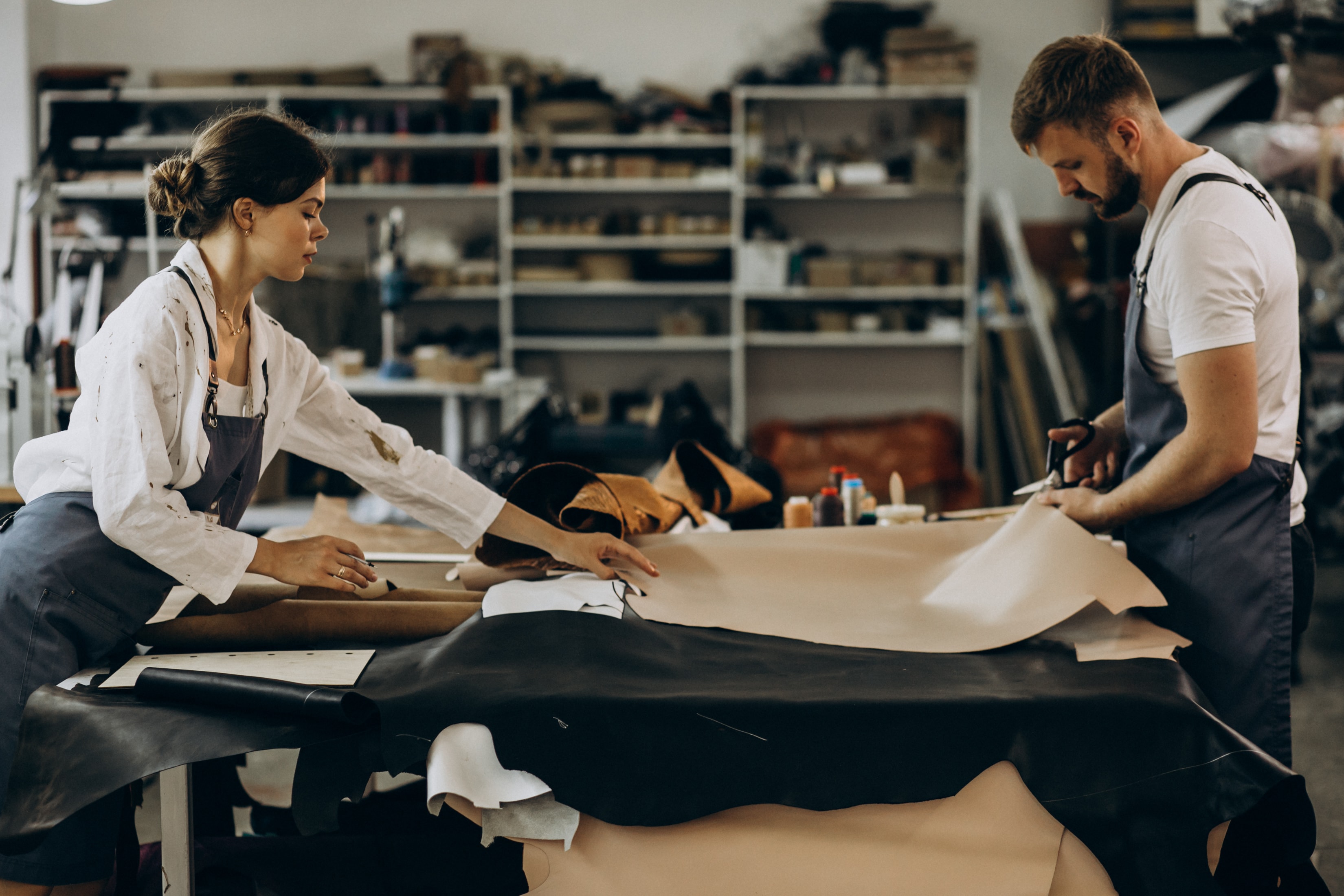 A man and a woman working on leather sheets in a factory