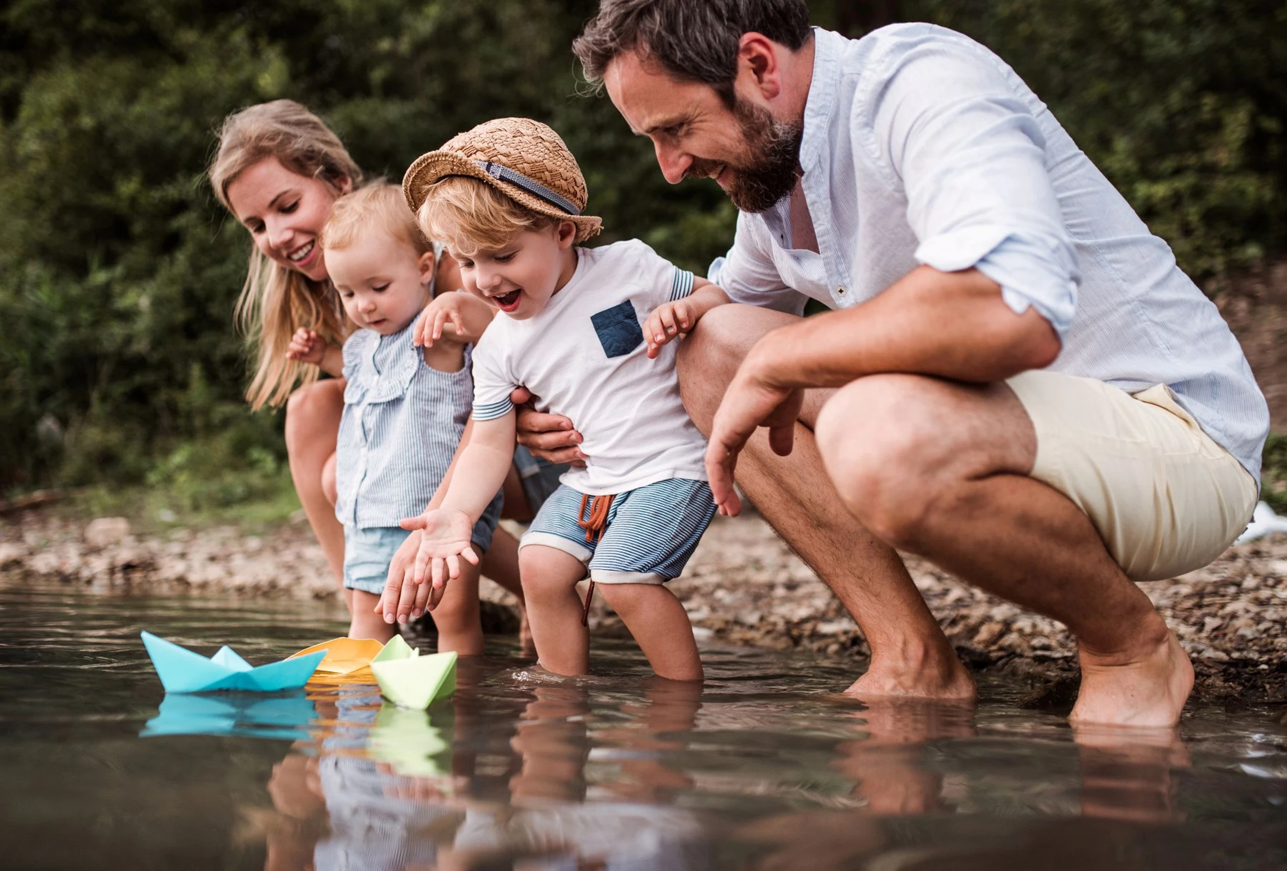 Young family with two toddler children outdoors by the river in summer, playing, by Halfpoint / Adoube Stock