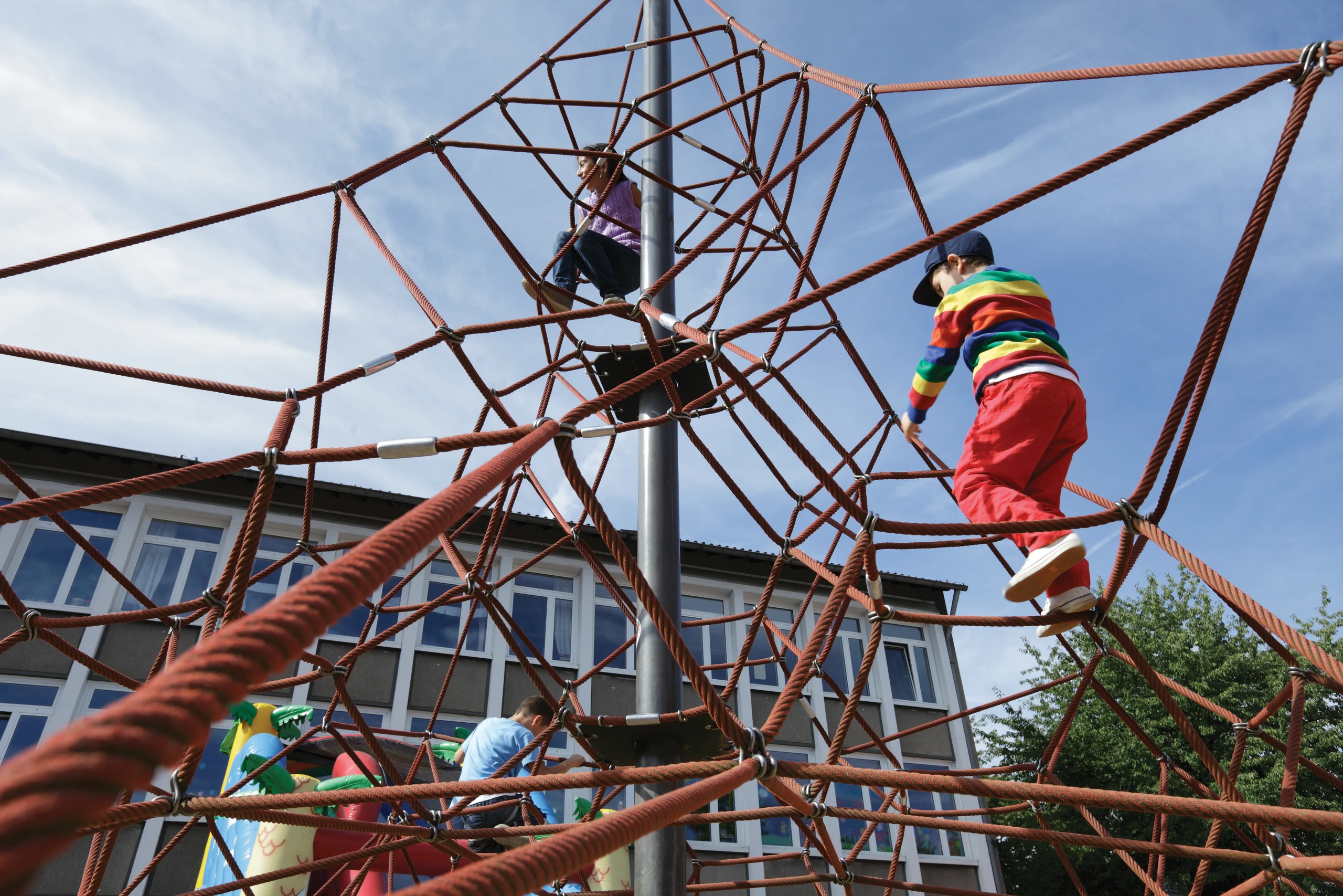 Kids play on a climbing frame in playground in front of apartment block