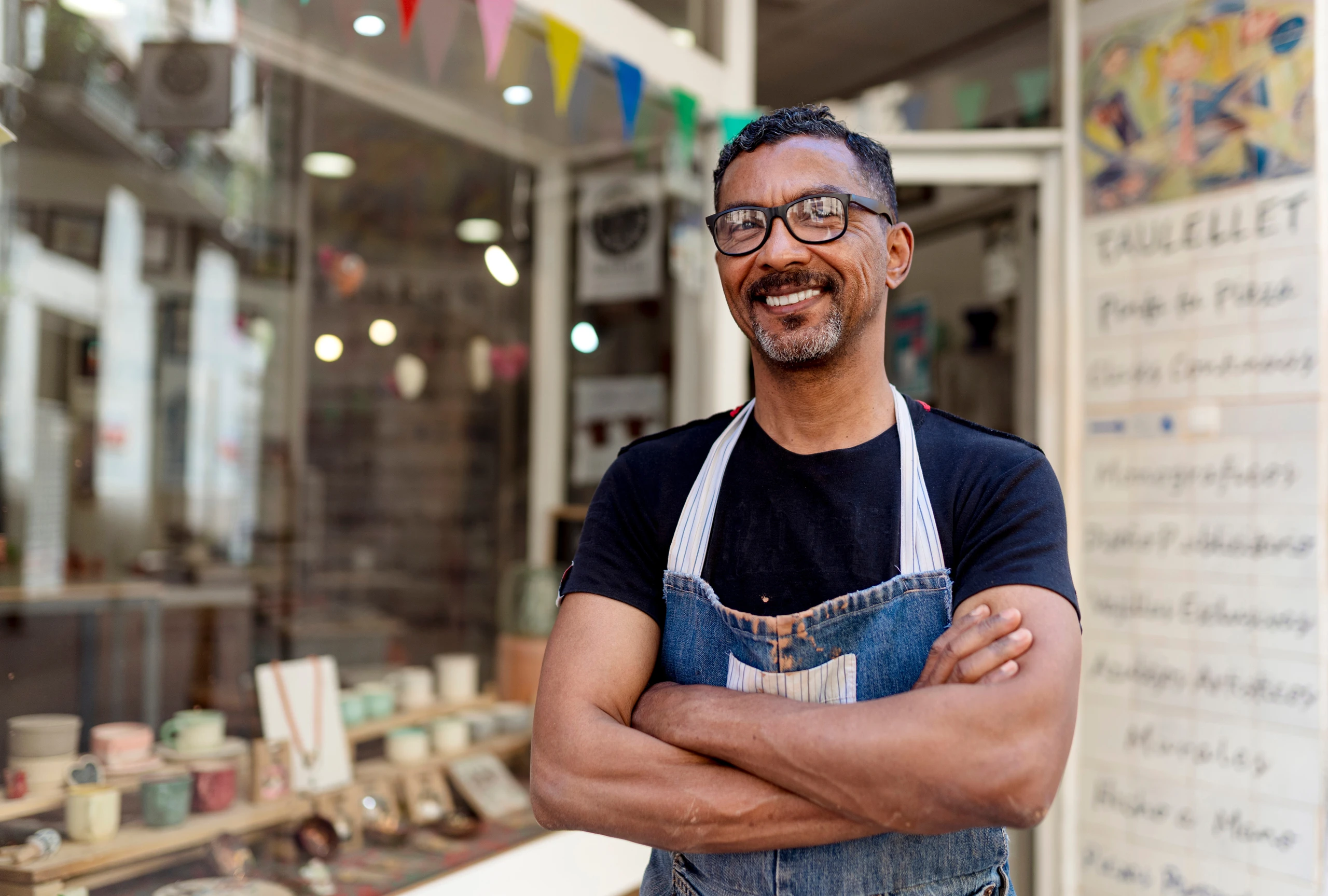 Confident male potter with arms crossed standing outside ceramic shop by tunedin / Adobe Stock
