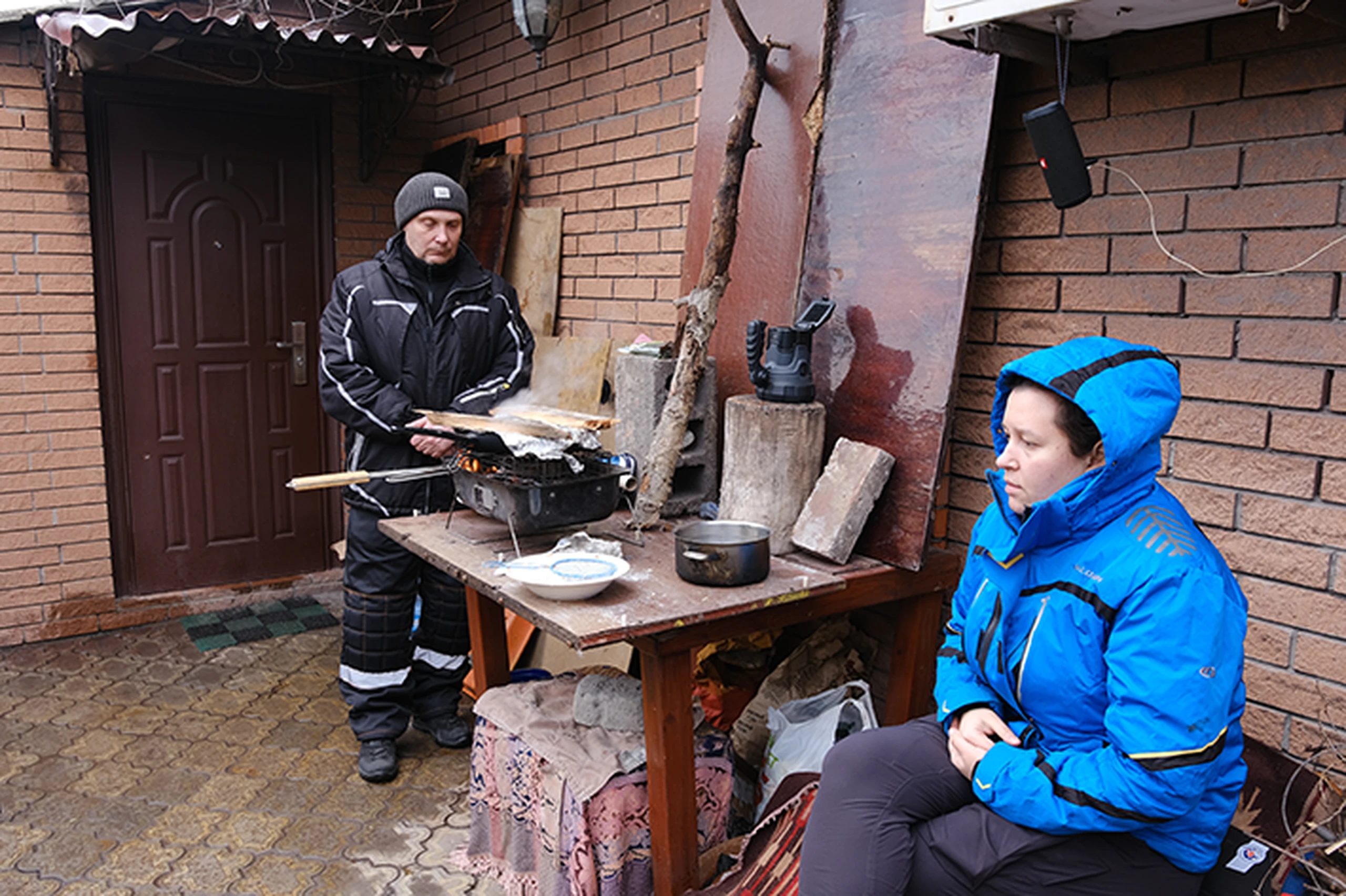 Image of family cooking around camp fire outside home under bombardment in Ukraine