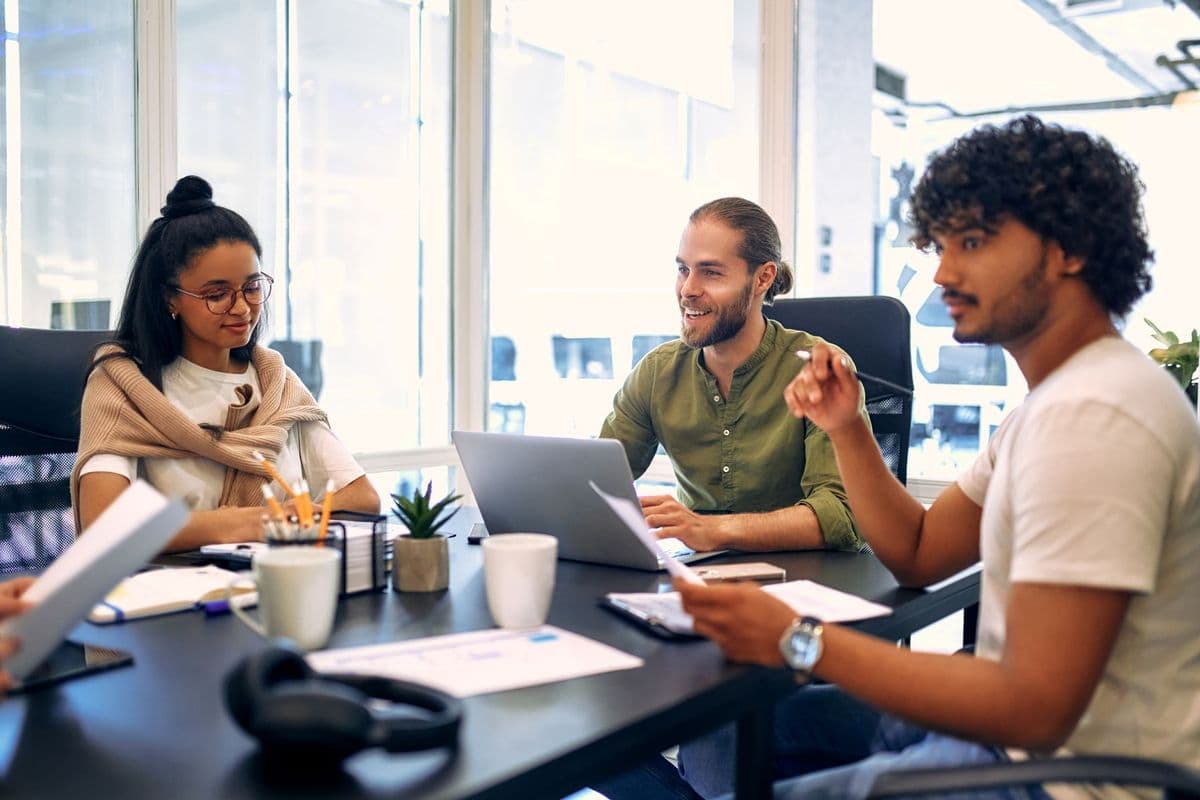 EWCS 2024 highlights digital story image - A group of people sitting around a table in a modern office, engaged in a meeting with laptops, papers, and coffee cups.