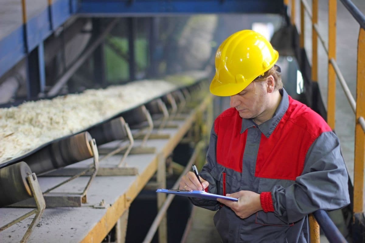 Worker in a yellow hard hat and red-gray uniform working in a sugar factory