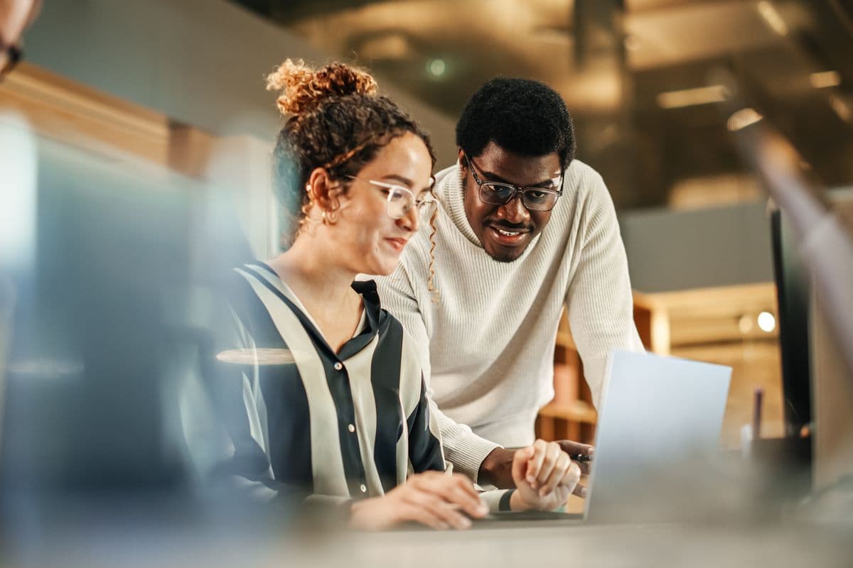 Portrait of Two Creative Colleagues Using Laptop to Discuss Work Project at Office