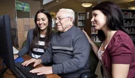 Volunteers teaching older man on computer