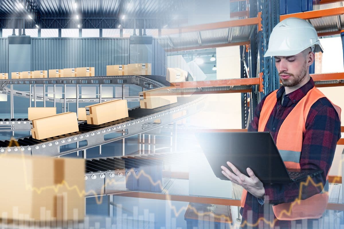 Mail warehouse worker monitors package conveyor system using a laptop.