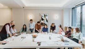 Group of people collaborating and brainstorming ideas around a large table in a bright, modern office environment
