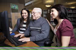 Image of volunteers teaching older man computers