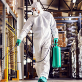 Image of man in protective suit and mask disinfecting warehouse full of food products