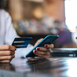 Image of woman paying for goods by credit card through a smartphone in a coffee shop