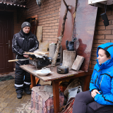 Image of family cooking around camp fire outside home under bombardment in Ukraine