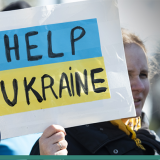 Image of female refugee holding a sign saying 'Help Ukraine'