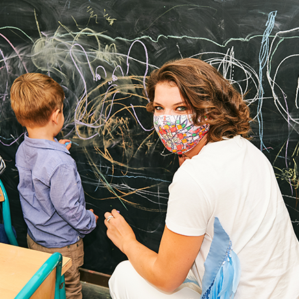 Image of a young female teacher drawing with a child on a chalk board